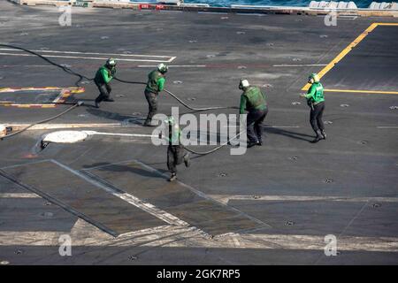 210829-N-CW176-1024 ARABIAN SEA (Aug. 29, 2021) – Sailors handle an arresting wire on the flight deck of aircraft carrier USS Ronald Reagan (CVN 76) in the Arabian Sea, Aug. 29. Ronald Reagan is the flagship for Carrier Strike Group 5 and is deployed to the U.S. 5th Fleet area of operations in support of naval operations to ensure maritime stability and security in the Central Region, connecting the Mediterranean and the Pacific through the western Indian Ocean and three strategic choke points. Stock Photo