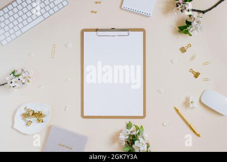Blogger workplace with glider, white apple flowers, gold stationery, computer, tablet with white blank note paper and pen on beige background with cop Stock Photo