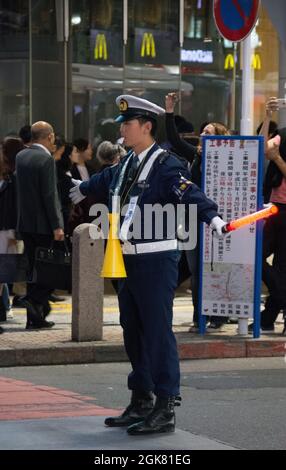 Japanese policeman with a glowstick, herding people along at the Shibuya Crossing to allow traffic to flow freely, Tokyo, Japan, October Stock Photo