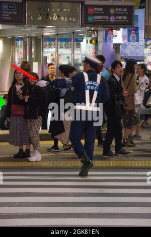 Japanese policeman with a glowstick, herding people along at the Shibuya Crossing to allow traffic to flow freely, Tokyo, Japan, October Stock Photo
