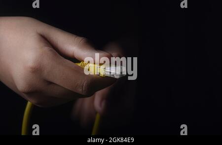 Front Hand holding a Yellow LAN Ethernet cable, and back hand out of focus on the Black ground. The conceptual idea for Artificial intelligence, science Stock Photo