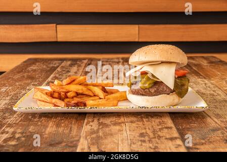 Beef burger with fried green peppers, tomato and onion slices and havarti cheese on top garnished with French fries Stock Photo