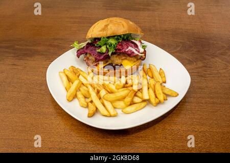 Beef burger with double cheddar cheese with caramelized onion with slices of fried bacon and lettuce and garnish of French fries Stock Photo