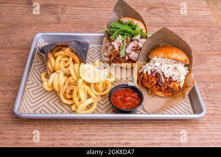 Tasting tray of two shredded beef and pork burgers with lots of fresh cheese, ruchula, barbecue tomato sauce and spiral fries Stock Photo