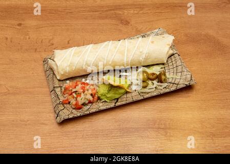 Large wheat tortilla burrito with salsa and garnishes of pico de gallo, ripe avocado guacamole with corn tortilla chips and lettuce with jalapeños Stock Photo