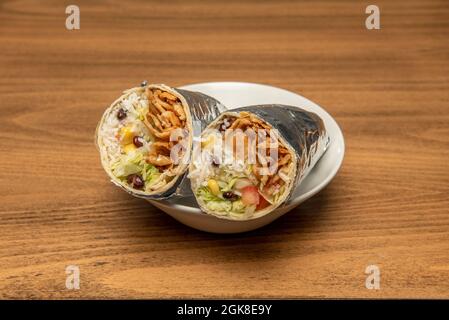 Super special stewed chicken burrito with sweet corn, white rice with black beans, lettuce and pico de gallo wrapped in aluminum foil cut in half Stock Photo