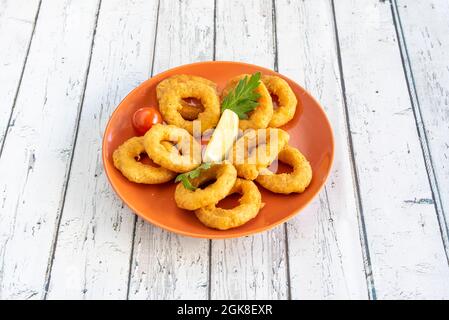 Tapa of battered processed squid on orange plate with lemon and parsley and white background Stock Photo