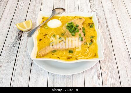 Typical Peruvian chicken broth with old chicken leg, assorted vegetables, noodles, boiled egg and a lot of boiling liquid on a light table Stock Photo