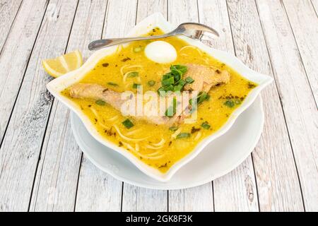 Square shaped bowl of Peruvian chicken broth recipe with noodles, chives and boiled egg on light wooden table Stock Photo