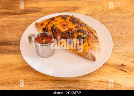 Italian calzone stuffed with ham, cheese and tomato, with more tomato sauce for drizzling Stock Photo