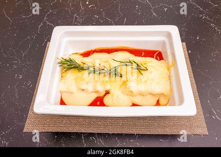 Tray of cannelloni stuffed with meat with grated cheese, béchamel sauce and baked tomato gratin Stock Photo