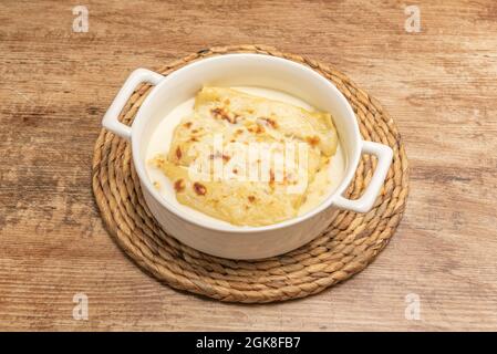 White porcelain tart pan with a portion of cannelloni stuffed with meat with béchamel sauce and grilled cheese Stock Photo