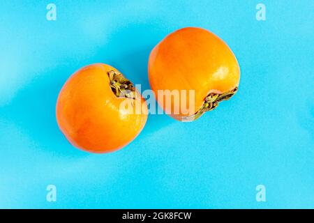 Two ripe persimmons keeping company on a blue background Stock Photo