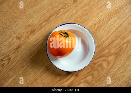 Ripe persimmon on white plate with blue edge on wooden table. Season's fruit Stock Photo