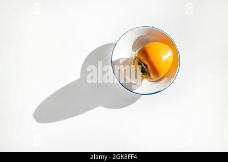 Ripe persimmon on white plate and long shadow on white table Stock Photo