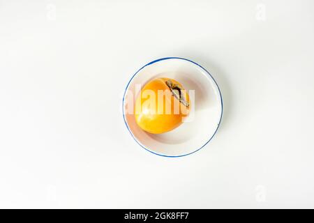 Ripe persimmon on white plate with blue border Stock Photo