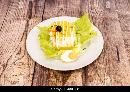 Typical Peruvian Causa Limeña presented in layers with yellow potatoes and salad filling with mayonnaise, boiled eggs and vegetables on a white plate Stock Photo