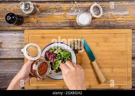 Woman's hands dressing salad in a white bowl on a bamboo board. Stock Photo