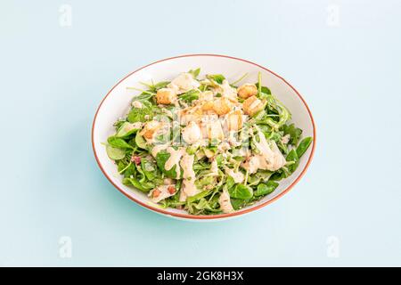 Bowl of caesar salad with lamb's lettuce, croutons, dried fruits and mayonnaise on blue background Stock Photo