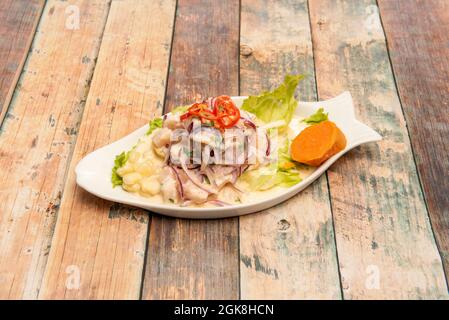 Peruvian corvina ceviche marinated with lime, onion, corn kernels, sweet potato and lettuce in a fish-shaped plate on wooden table Stock Photo