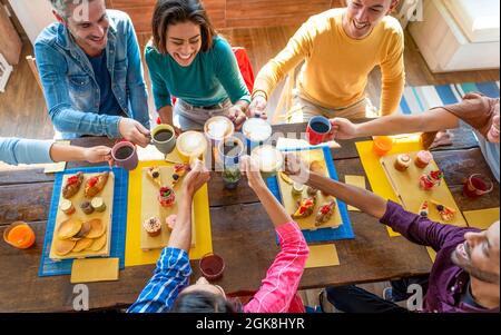 cropped top. multiethnic group of friends sitting on a table in a bar restaurant making a cheers with cappuccino and coffee. diverse people celerating Stock Photo