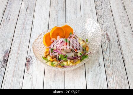Peruvian corvina ceviche with red onion, parsley, sweet potato slices in a beautiful glass bowl with corn grains Stock Photo
