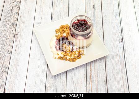 Cheesecake in a glass jar with red berry jam and biscuit soil
