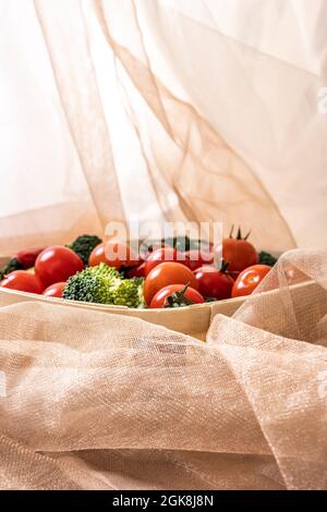 Wooden basket with cherry tomatoes and chopped broccoli surrounded by pink tulle fabric with sparkles. Stock Photo