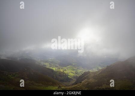 From above of picturesque green hills and valley under thick gray clouds with sunlight Stock Photo