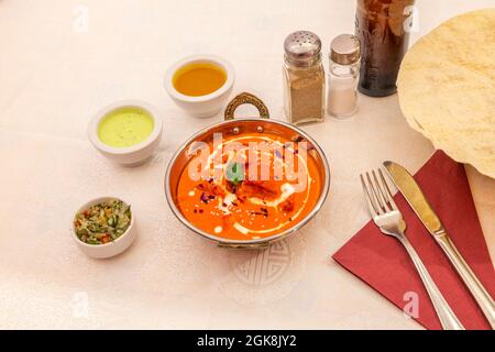 Indian recipe of chicken tikka masala with cream in traditional bowl on white tablecloth with sauces and accessories Stock Photo