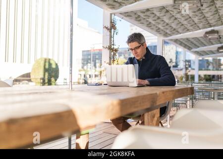 Young male in trendy outfit browsing netbook while working on project on street Stock Photo
