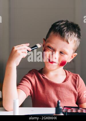 Charming child with makeup applicator looking away at table with eyeshadow palette Stock Photo