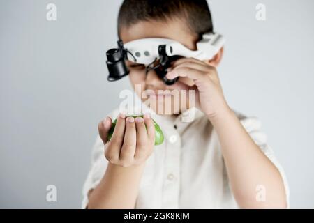 Little boy holding a slime and looking on it through the special magnifying eyeglasses headset Stock Photo