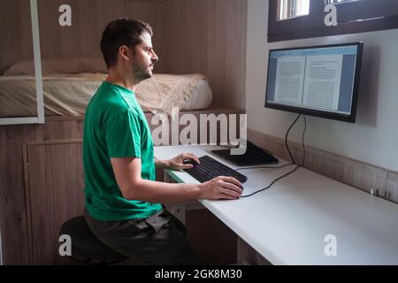 Side view of male blogger in eyeglasses editing text on monitor while typing on keyboard in house room Stock Photo