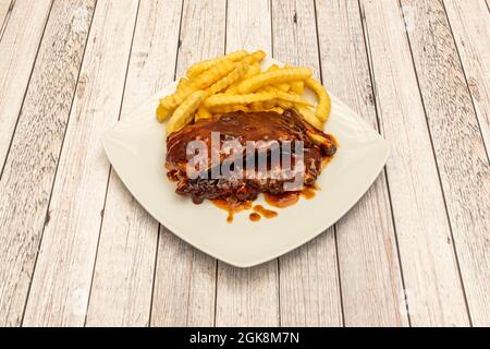 Pork ribs that melt in your mouth with barbecue sauce and portion of chips on a white plate Stock Photo