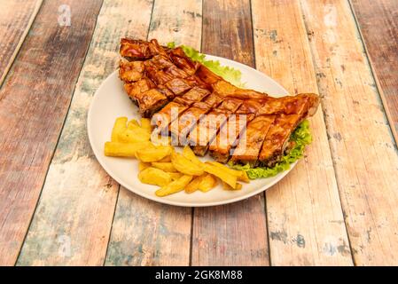 Pork ribs marinated in sauce and cooked on grill with homemade chips on wooden table Stock Photo