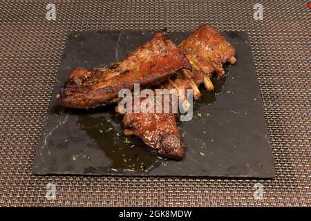 Delicious barbecued ribs seasoned with parsley, pepper, garlic and salt on a square black slate plate Stock Photo
