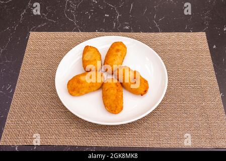 ration of croquettes battered with bread and egg, stuffed with béchamel and serrano ham on a plastic tablecloth Stock Photo