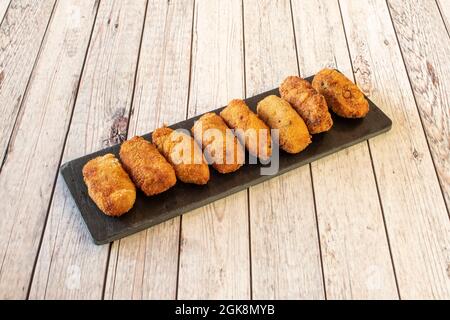 Group of homemade croquettes flavored with cod well fried and breaded in bread on black rectangular slate and white table Stock Photo