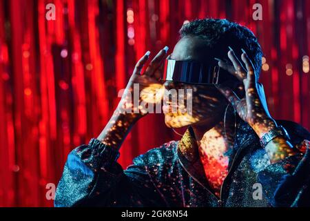 Trendy young black female in cyberpunk glasses with shadows on face in light beams in nightclub Stock Photo