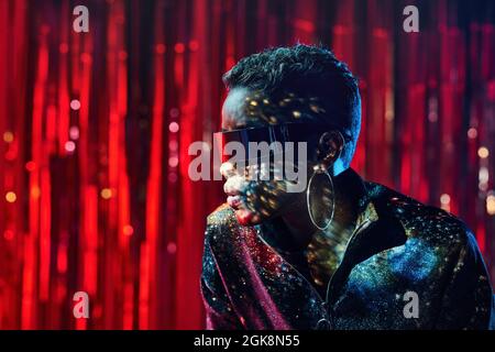 Trendy young black female in cyberpunk glasses with shadows on face in light beams in nightclub Stock Photo