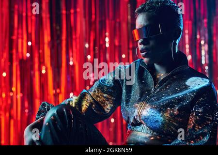 Trendy young black female in cyberpunk glasses with shadows on face in light beams in nightclub Stock Photo