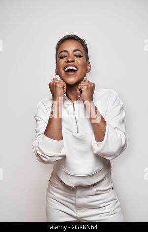 Positive young African American female in stylish apparel with makeup and short hair on light background Stock Photo