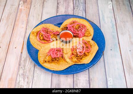 four Mexican corn tortilla tacos with a recipe for a cochinita pibil stew with red onion and dip sauce on a blue enameled plate Stock Photo