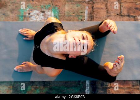 Young slender female in sports clothes doing Raja Bhujangasana while practicing yoga in city on sunny day Stock Photo