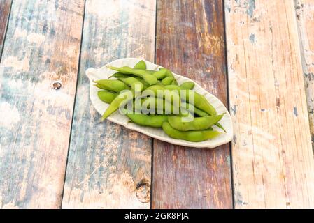 Small leaf shaped tray holding portion of Asian edamame in pod with some sea salt on wooden table Stock Photo