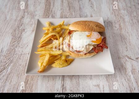 Classic beef burger with fried egg, lots of bacon and melted cheese with a side of homemade chips Stock Photo