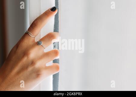 Closeup view of anonymous Woman hand with rings opening the curtains Stock Photo