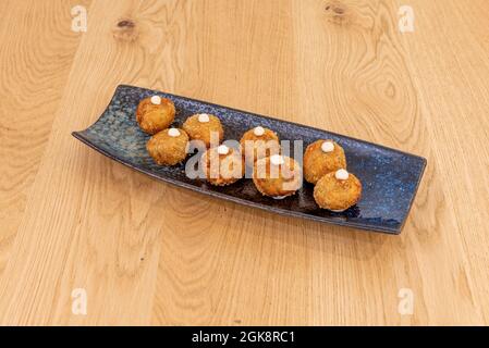 Black tray with round Spanish croquettes stuffed with ham and mushrooms topped with a dot of fresh cheese on an oak wood table Stock Photo