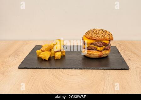 Double beef burger with lots of melted cheddar cheese and side of diced french fries on black slate plate Stock Photo